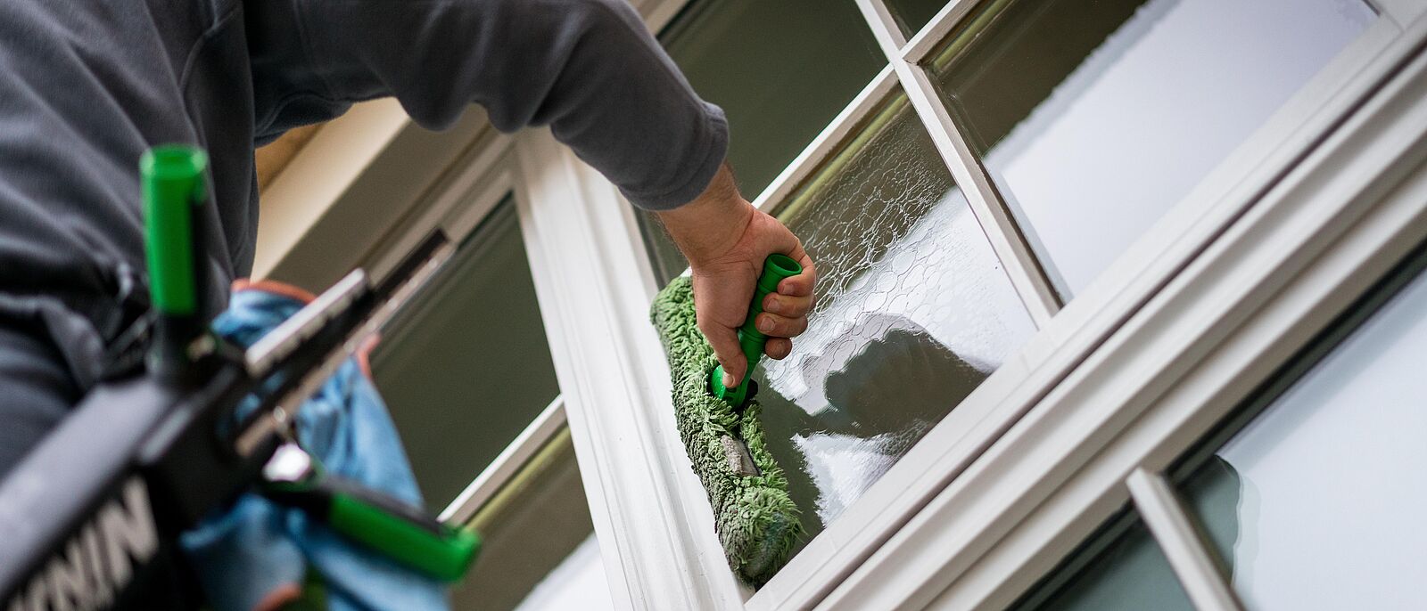 An einer Fensterfront reinigt gerade eine Person das Fenster.