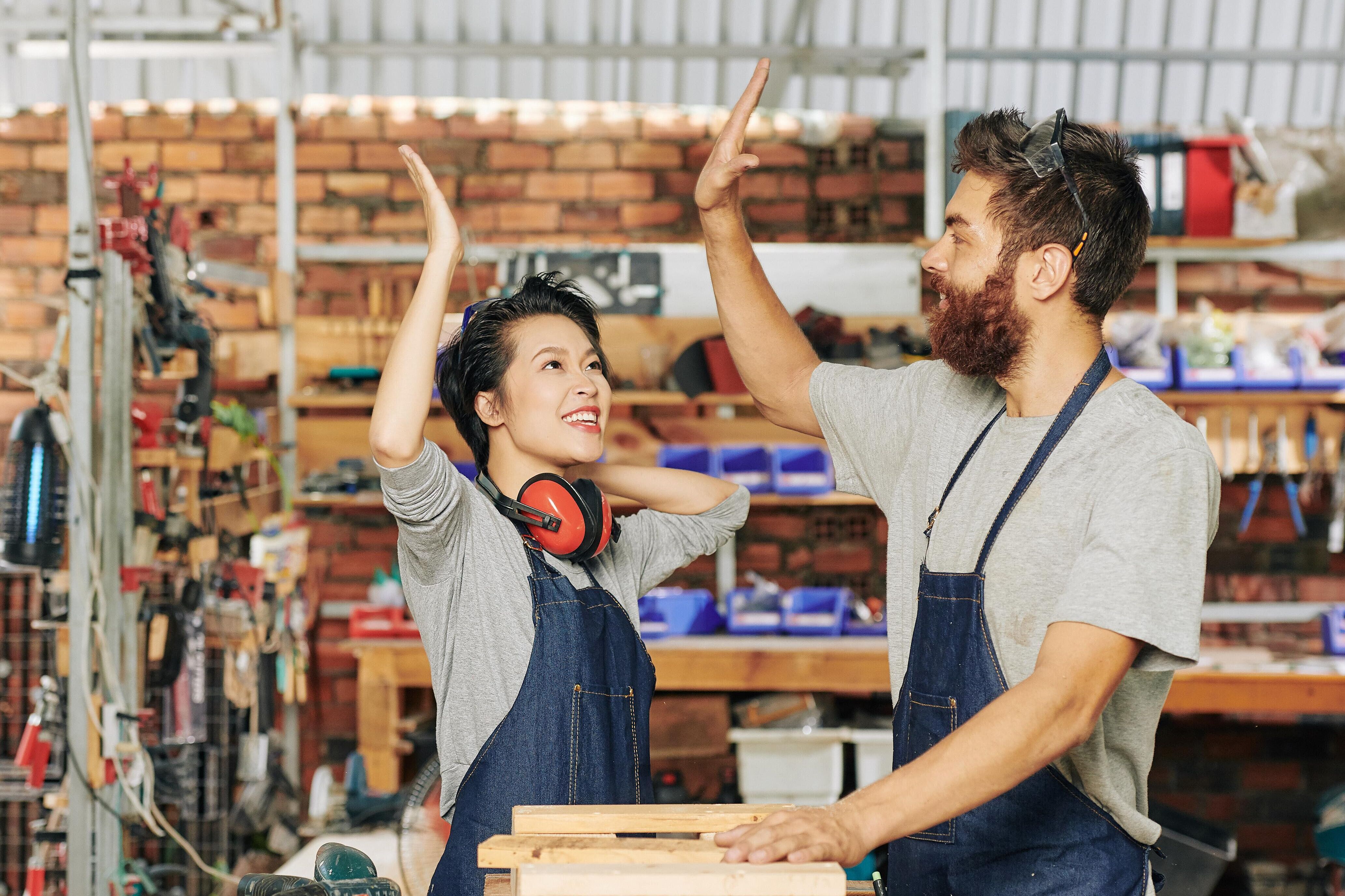 Du bist auf der Suche nach dem richtigen Ausbildungsberuf? Zwei Personen stehen in einer Tischlerwerkstatt und geben sich \"high five\".