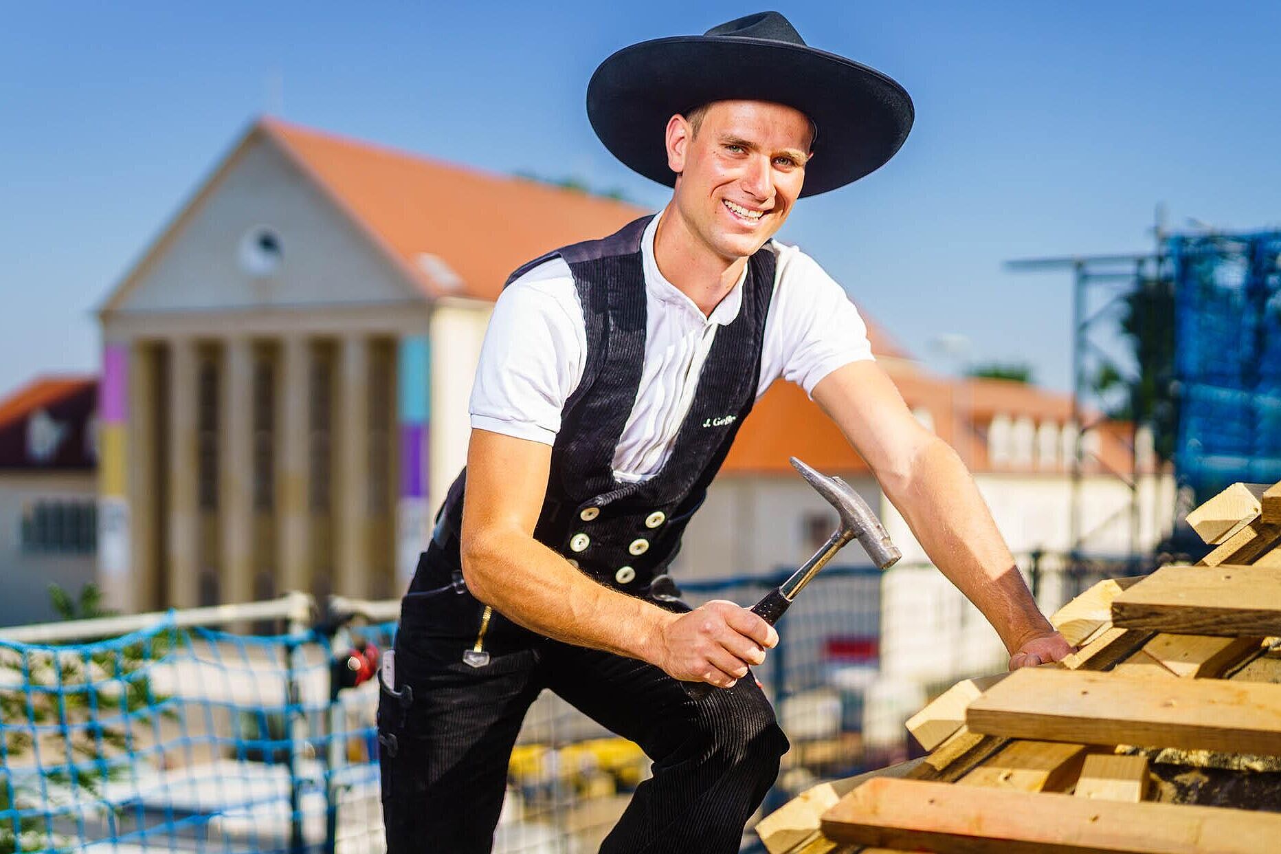 Ein Zimmermeister steht auf dem Dach und führt mit seinem Zimmererhammer Arbeiten aus.