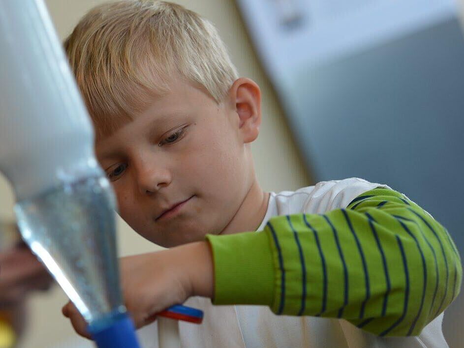 Ein Junge experimentiert mit verschiedenen Flüssigkeiten in Flaschen die mit den Flaschenhälsen aufeinander zusammengestellt wurden.