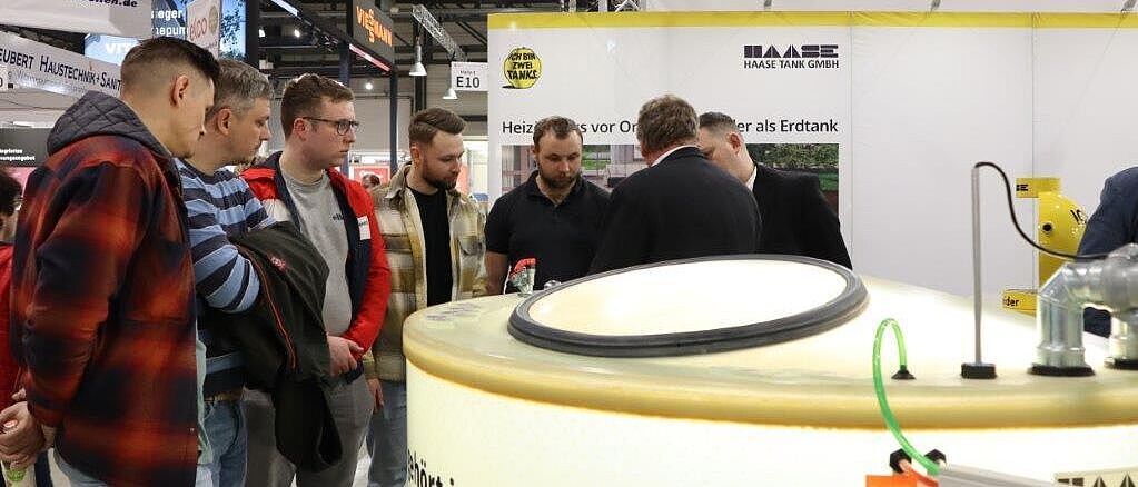 Mehrere Personen stehen an einem Messestand der Firma \"Haase Tank GmbH\" und führen angeregt eine Diskussion.