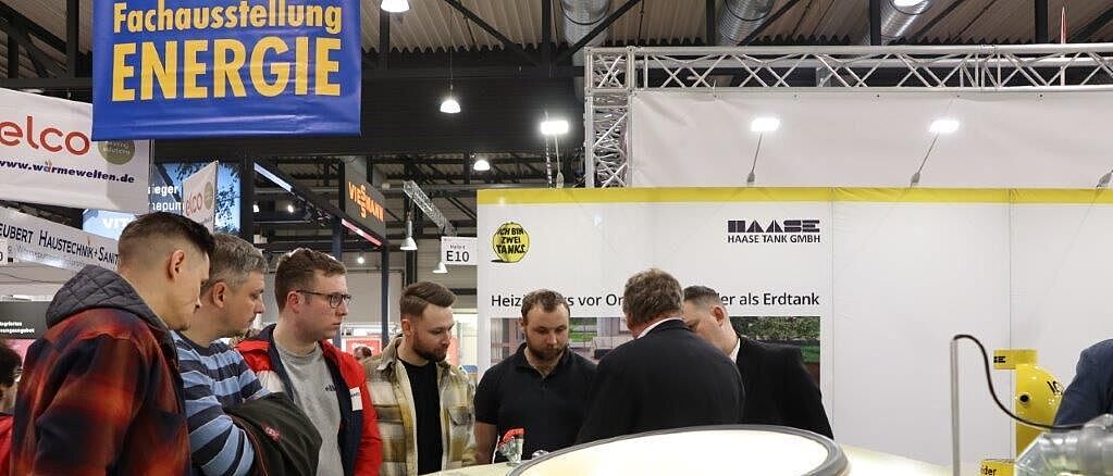 Mehrere Personen stehen an einem Messestand der Firma \"Haase Tank GmbH\" und führen angeregt eine Diskussion.