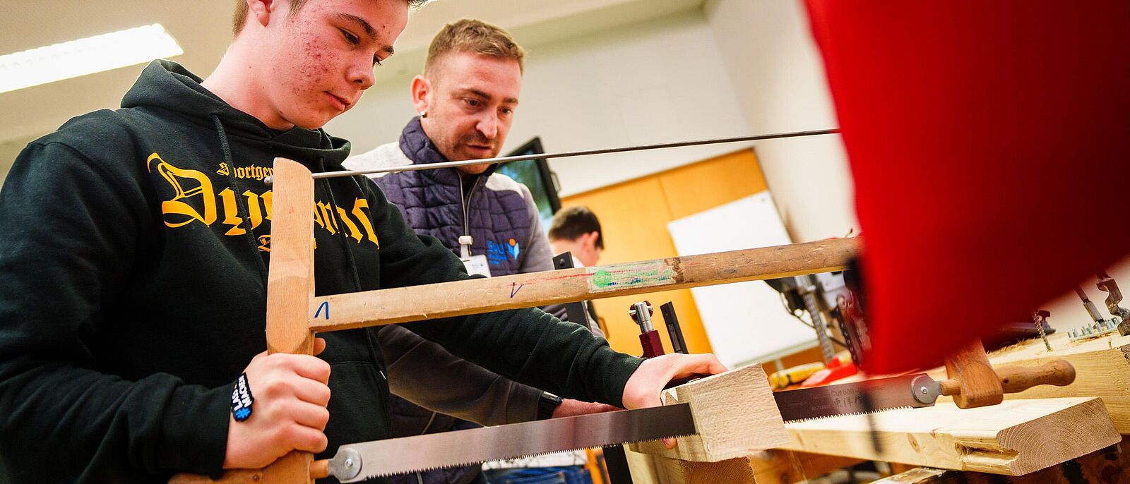 Bereichsleiter Ausbildung bei Bau Bildung Sachsen, zeigt Diego Sonntag von der 25. Oberschule den Umgang mit einer Gestellsäge.